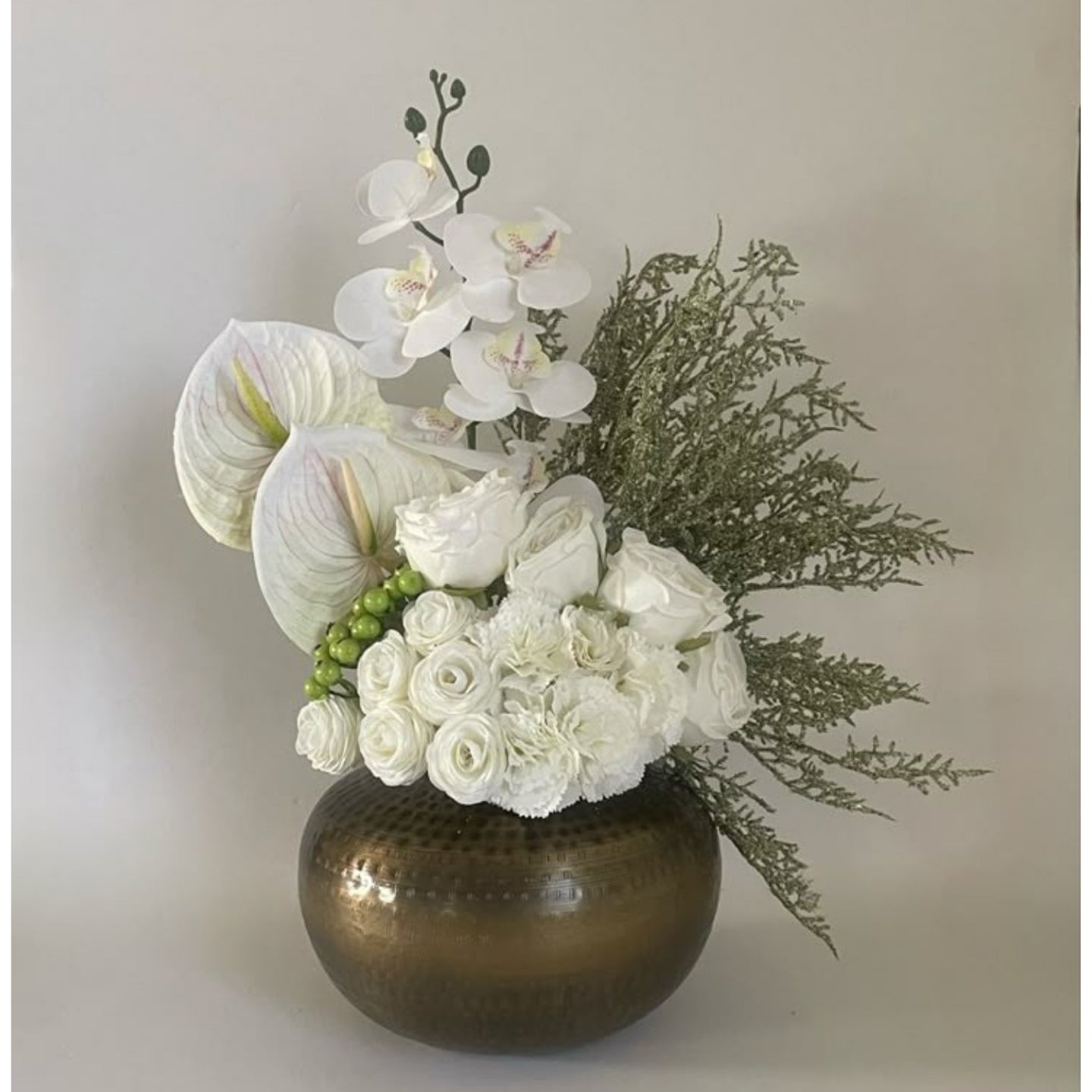 Floral arrangement with white flowers and greenery in a bronze vase on a light background