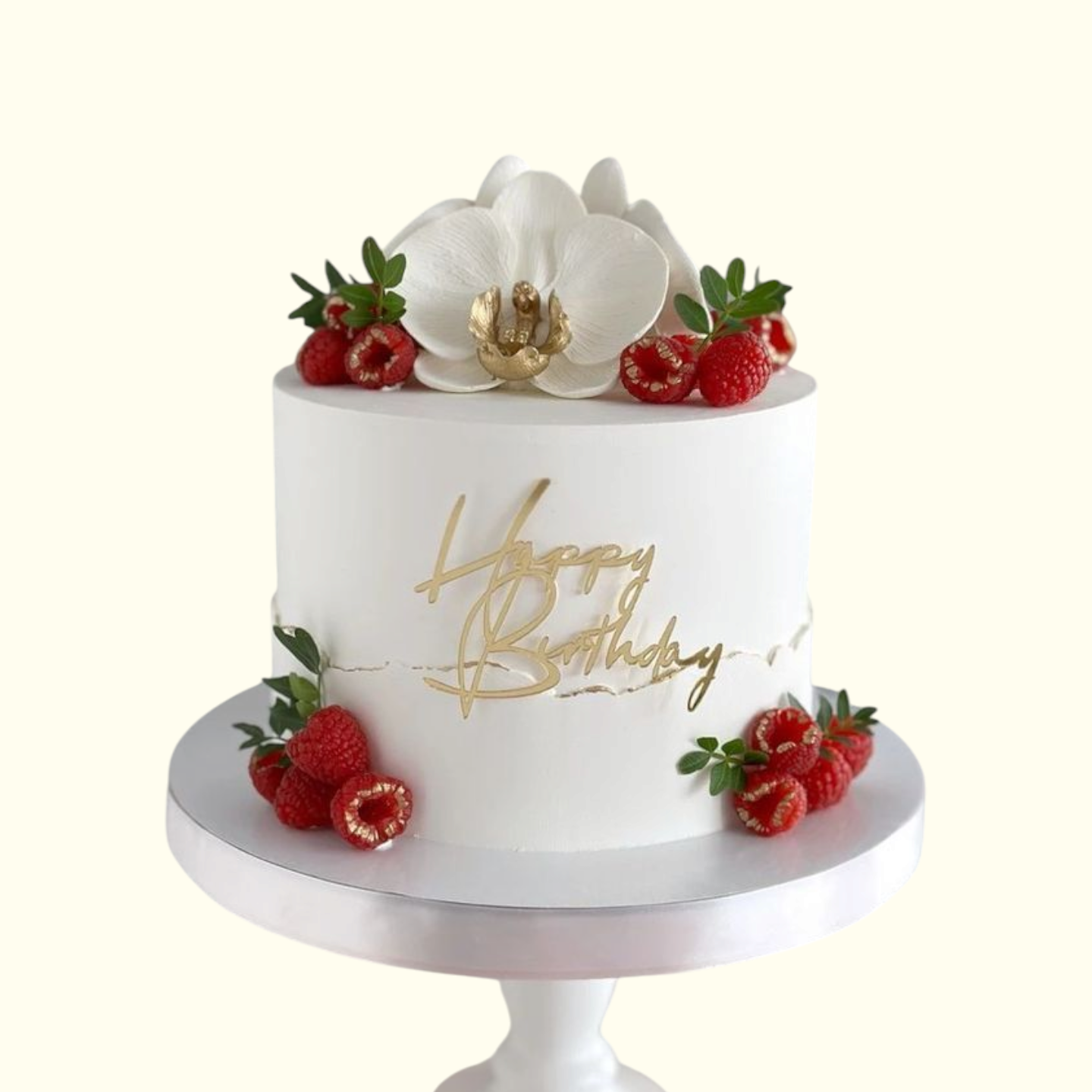 White birthday cake with gold 'Happy Birthday' text, white orchid, and red berries on a white background