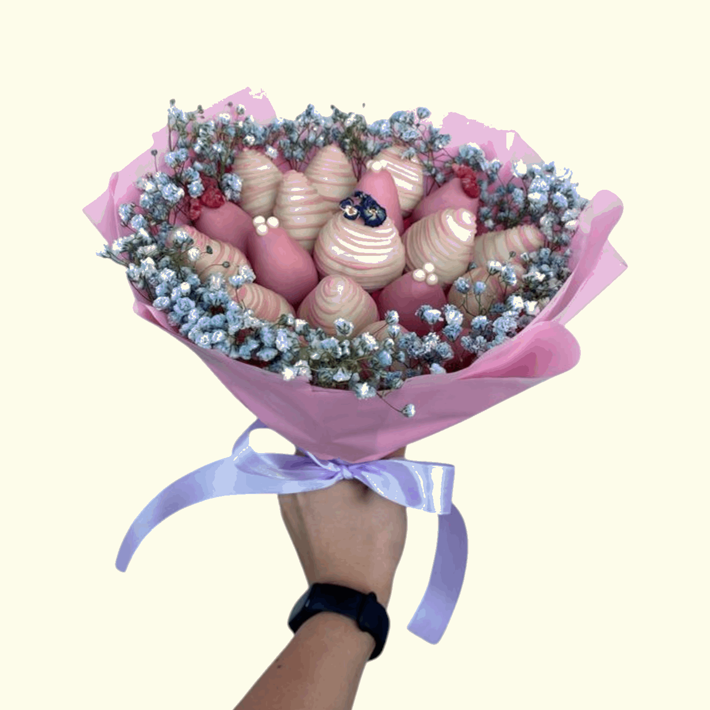 Bouquet of chocolates and flowers wrapped in pink paper with a hand holding it.
