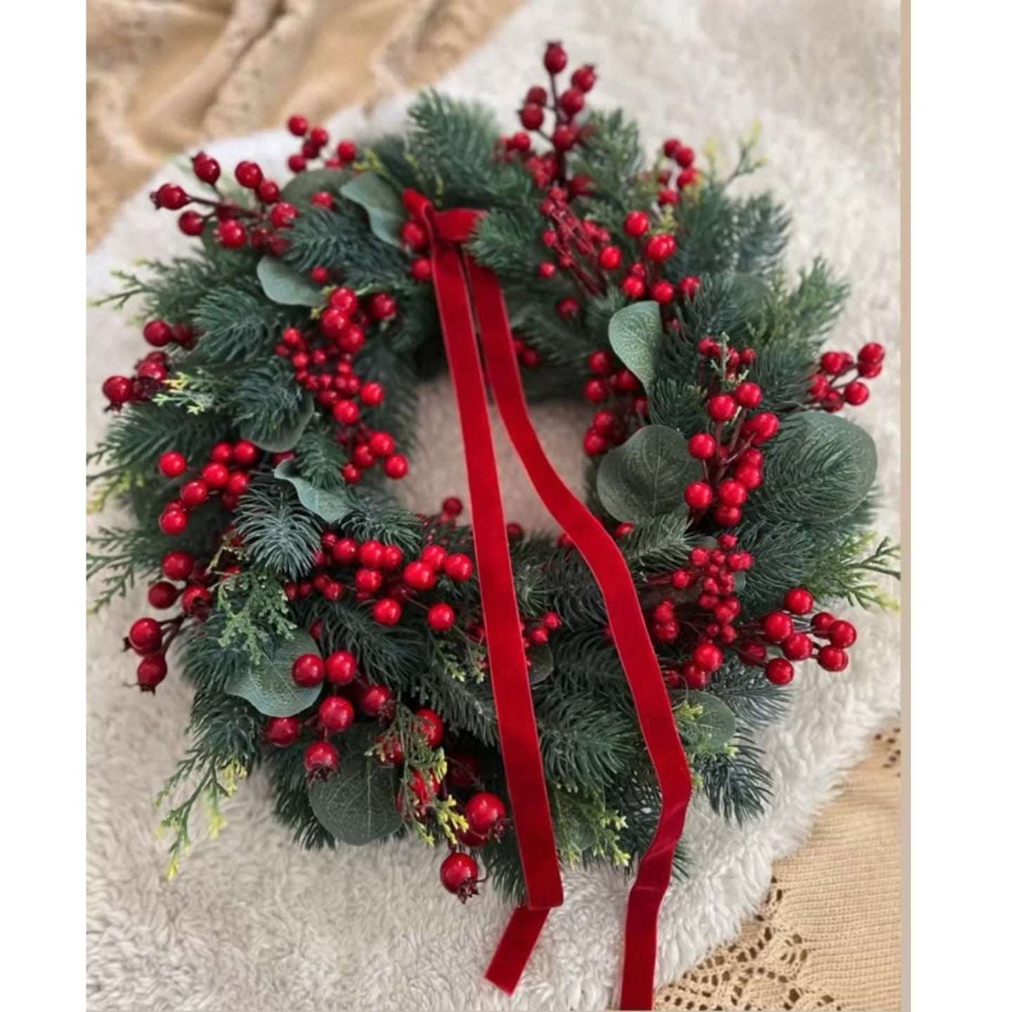 Christmas wreath with red berries and a red ribbon on a textured surface