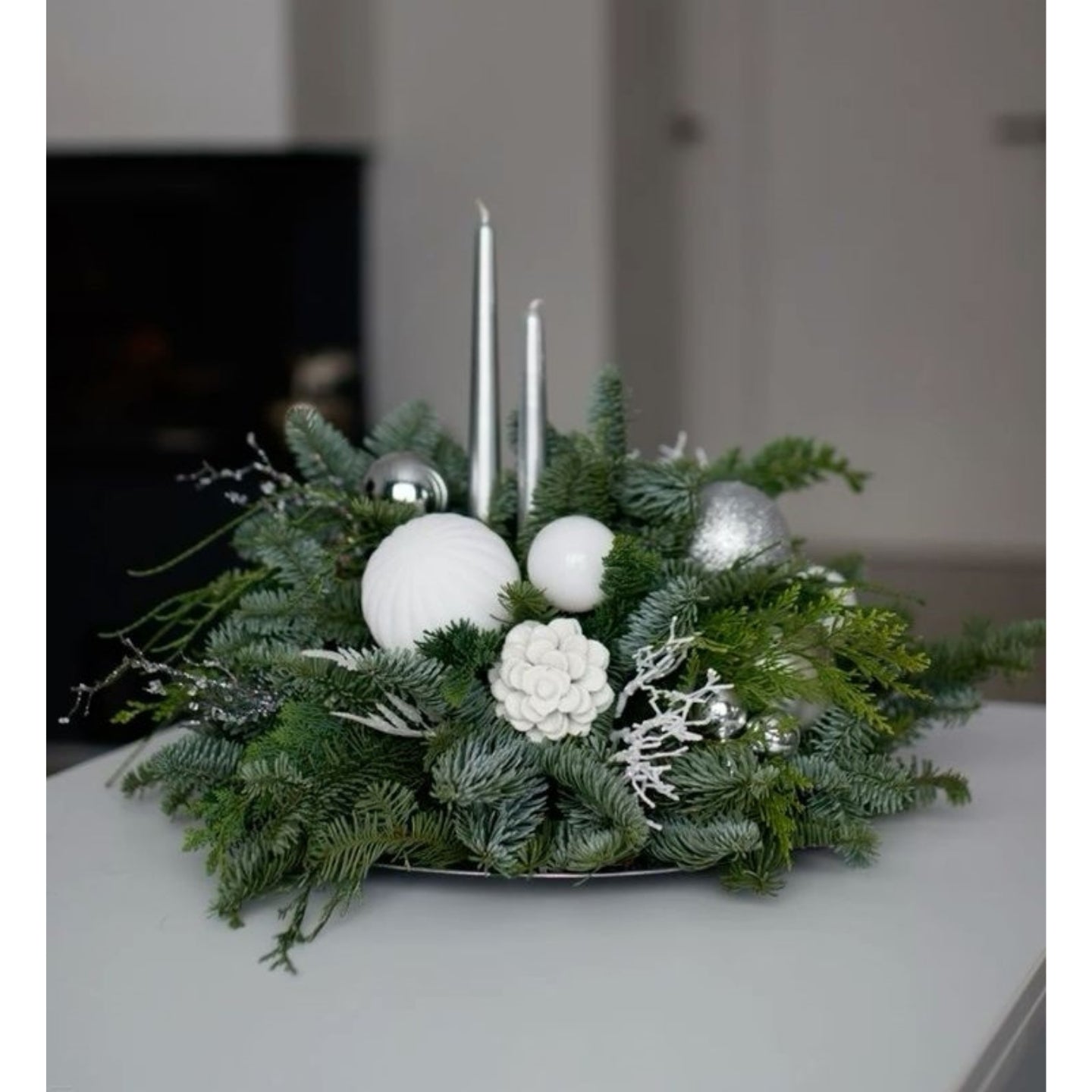 Christmas centerpiece with greenery, white ornaments, and candles on a neutral background