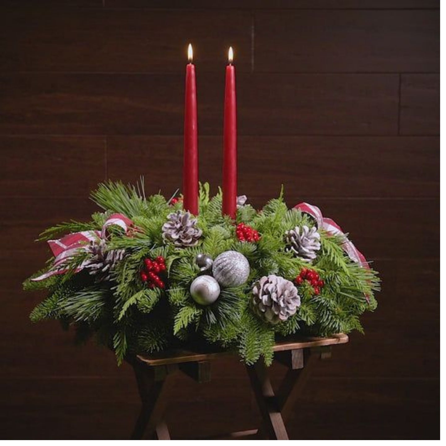 Decorative Christmas arrangement with red candles, greenery, and festive decorations on a wooden stand.
