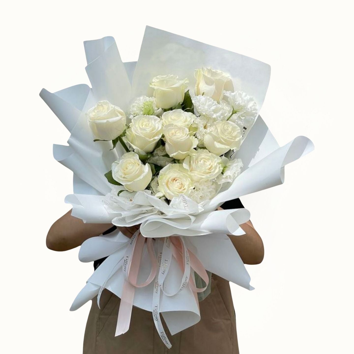 Bouquet of white roses wrapped in white paper with a pink ribbon held by a person.