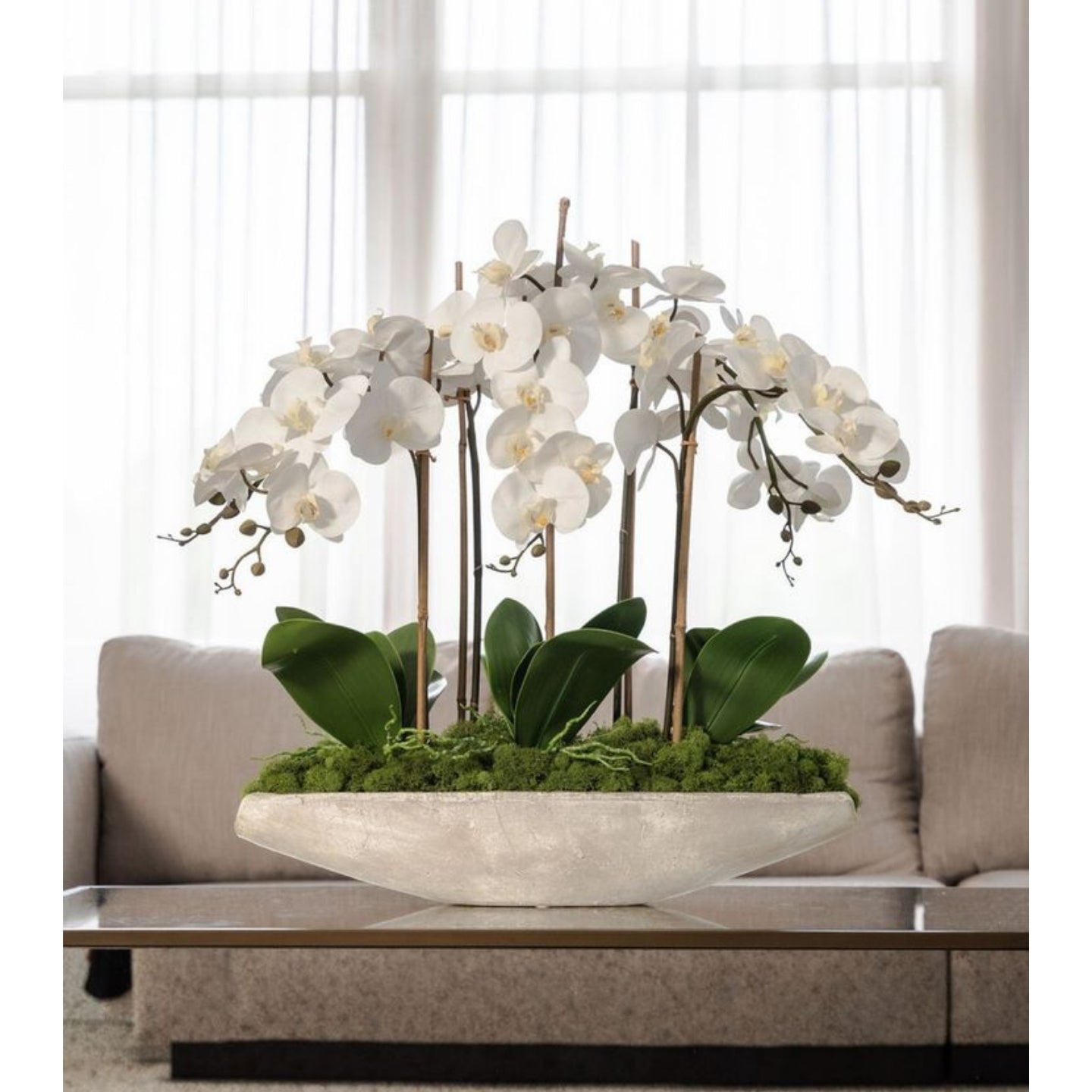 Decorative flower arrangement with white flowers and green leaves in a bowl on a coffee table.