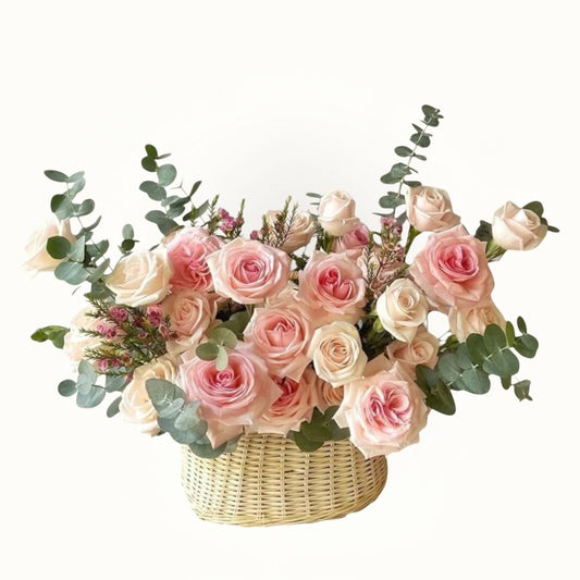 Bouquet of pink and white roses with greenery in a woven basket on a white background