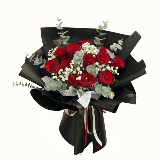 Bouquet of red roses with greenery wrapped in black paper and ribbon 