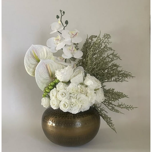 Floral arrangement with white flowers and greenery in a bronze vase on a light background