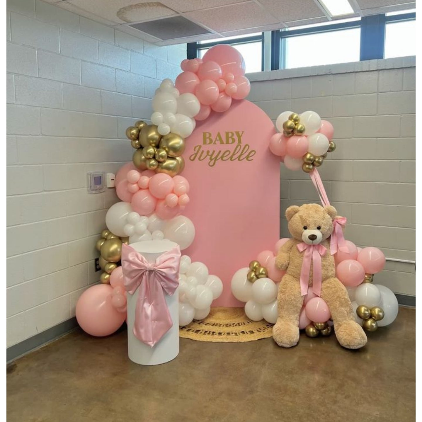 Baby shower setup with pink balloon arch, teddy bear, and 'Baby Juvyelle' sign.