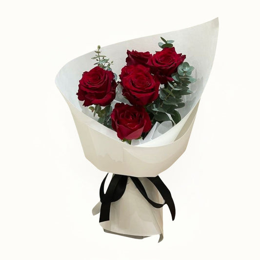 Bouquet of red roses with greenery wrapped in white paper and black ribbon on a white background