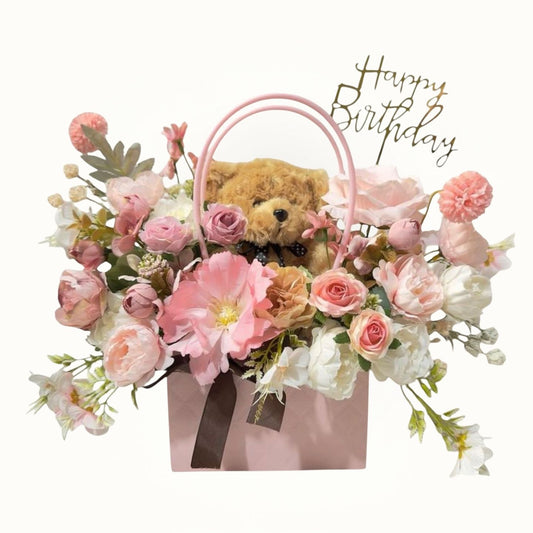 Teddy bear in a pink gift bag with flowers and 'Happy Birthday' text 