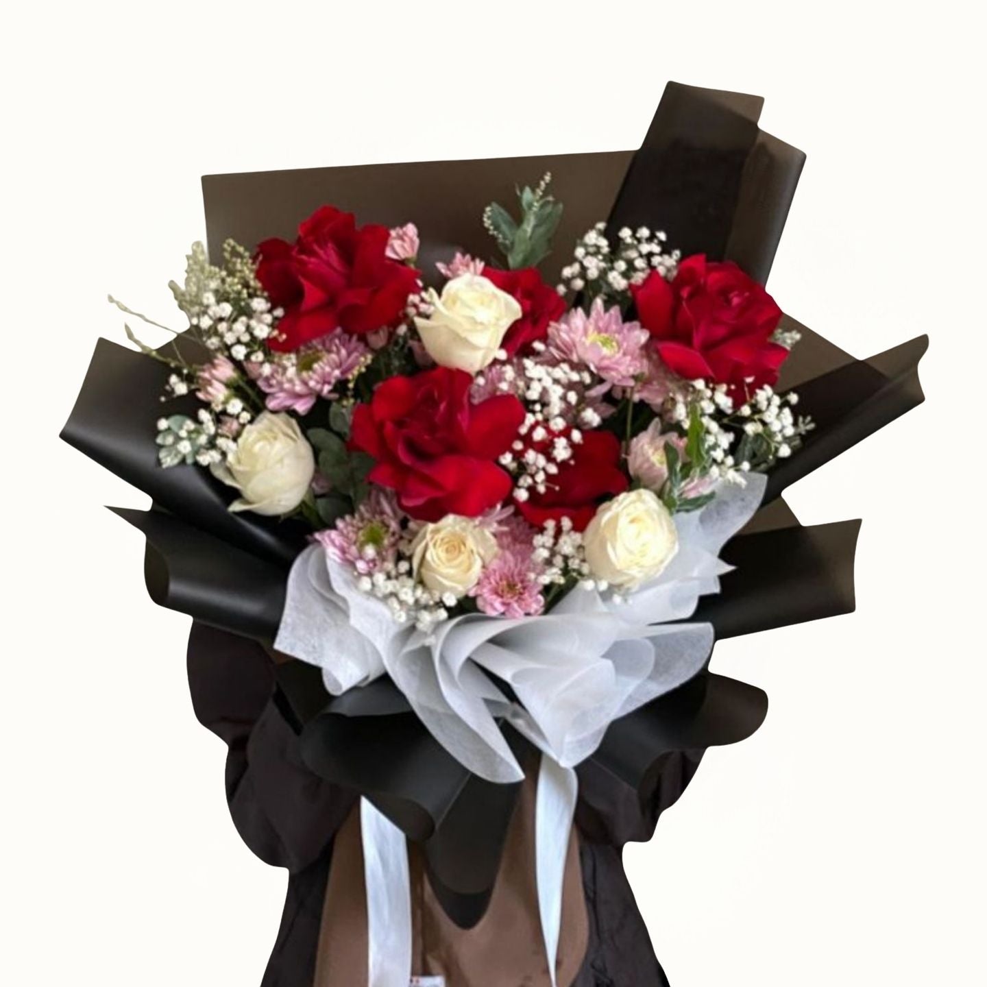 Bouquet of red, white, and pink flowers wrapped in black paper with a white ribbon on a white background.