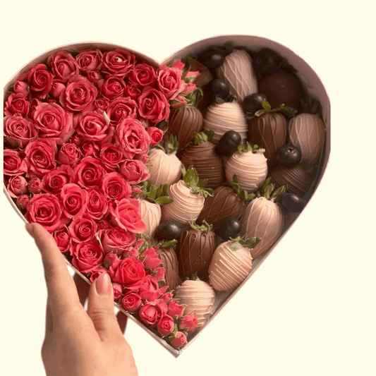 Heart-shaped box filled with red roses and chocolate-covered strawberries on a white background