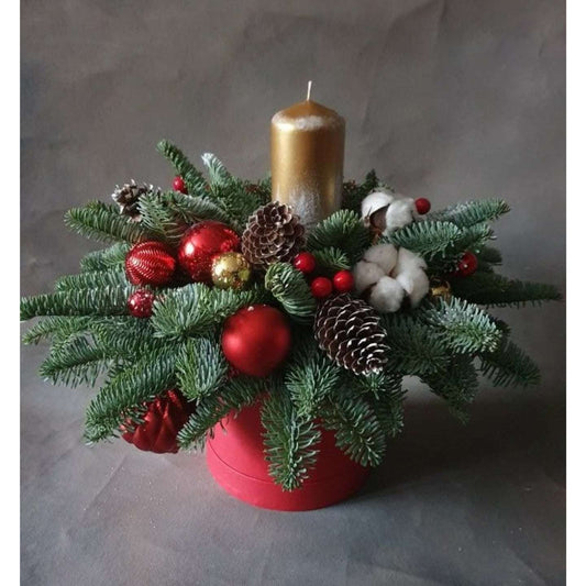 Decorative Christmas arrangement with a gold candle, red ornaments, and greenery on a gray background