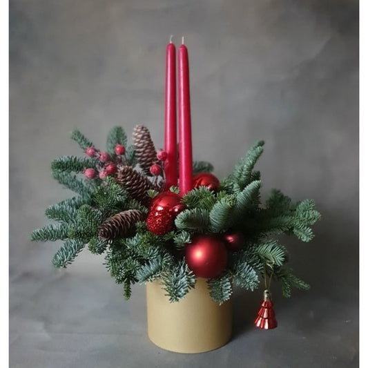 Decorative arrangement with red candles, pine cones, and ornaments on a neutral background