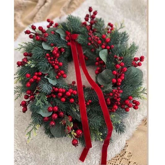 Christmas wreath with red berries and a red ribbon on a textured surface