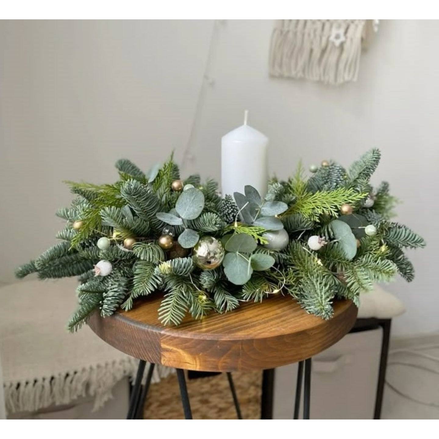 Decorative table centerpiece with greenery, small gold balls, and a white candle on a wooden table.