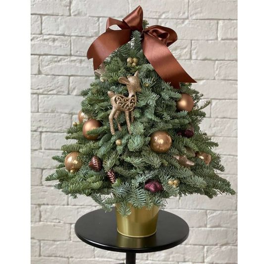 Decorated Christmas tree with gold ornaments and a brown ribbon against a white brick wall.