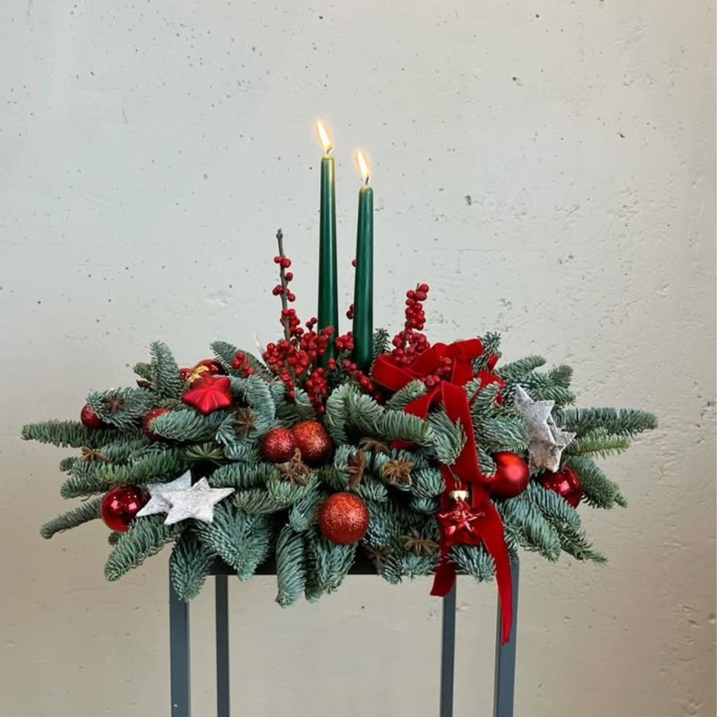 Decorative Christmas arrangement with candles, red ribbons, and ornaments on a neutral background