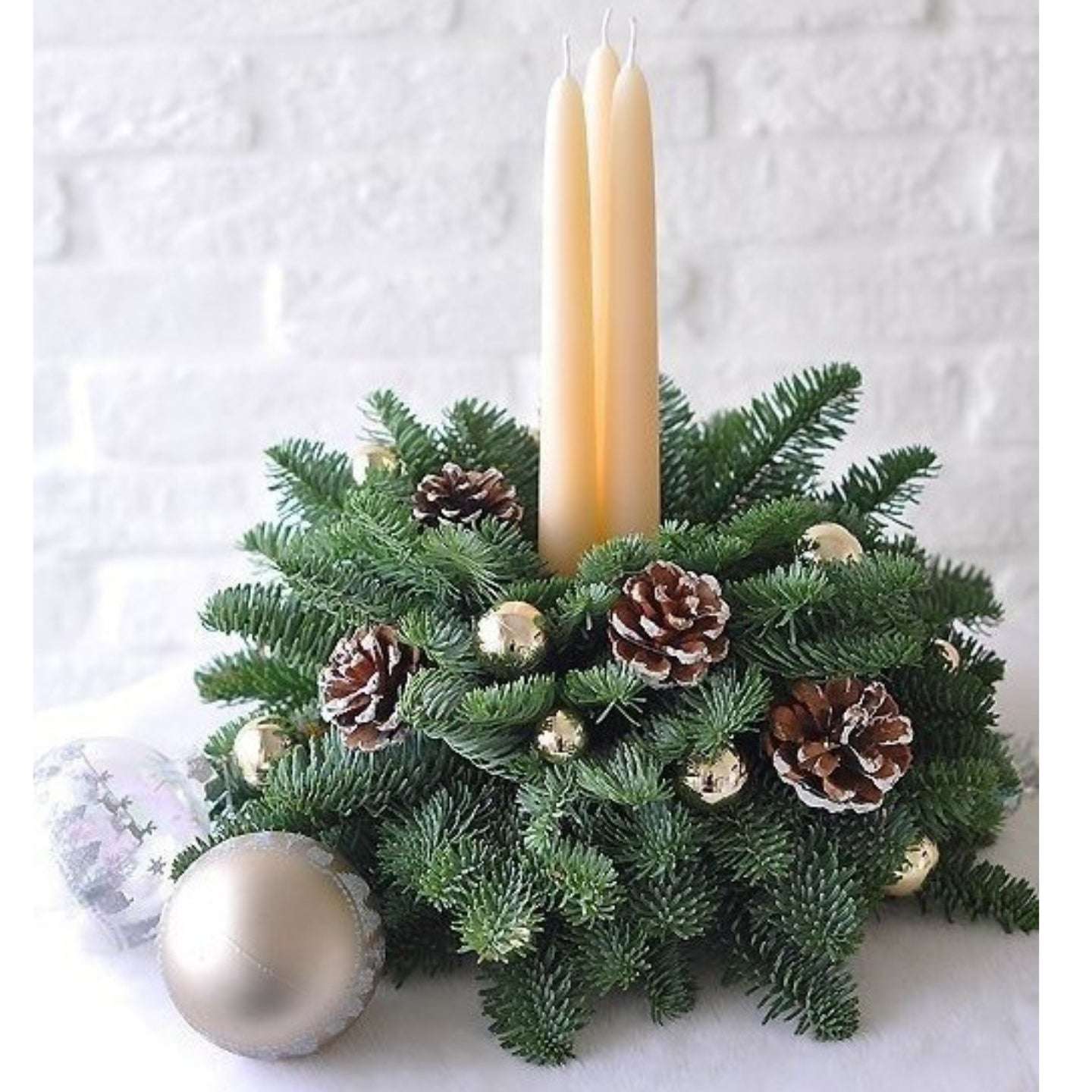 Decorative Christmas arrangement with candles, pinecones, and ornaments on a white background