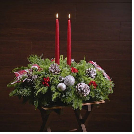 Decorative Christmas arrangement with red candles, greenery, and festive decorations on a wooden stand.