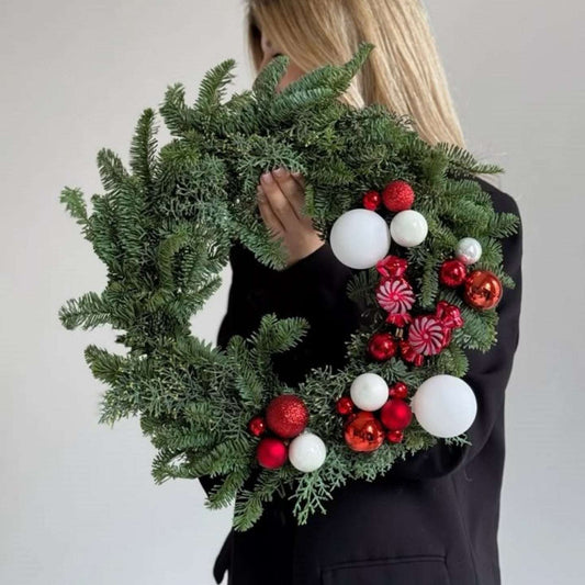 Person holding a Christmas wreath with red and white ornaments against a plain background