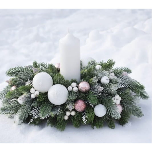 Decorative Christmas arrangement with a candle surrounded by greenery, ornaments, and white snow on a snowy background.