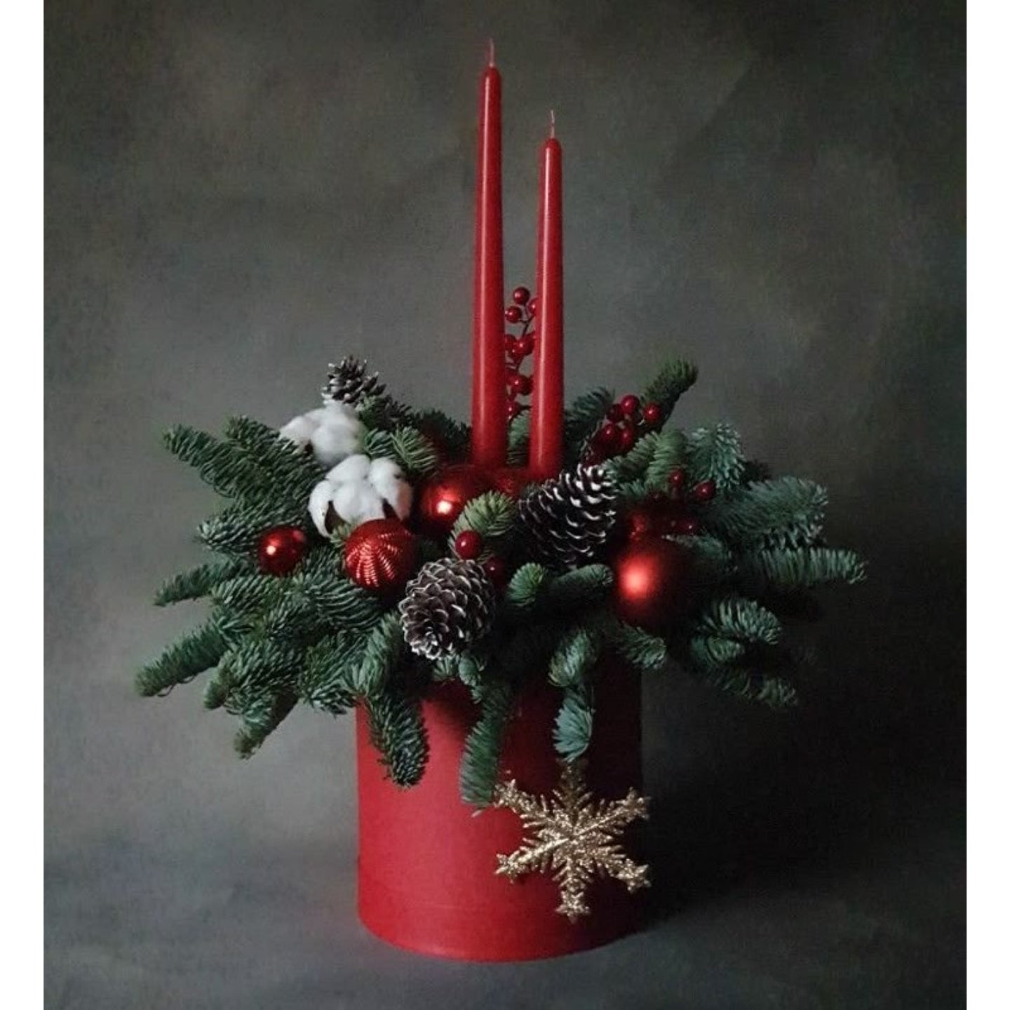 Decorative arrangement with red candles, pine cones, and berries on a dark background