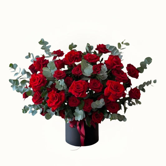 Bouquet of red roses with greenery in a black container on a white background