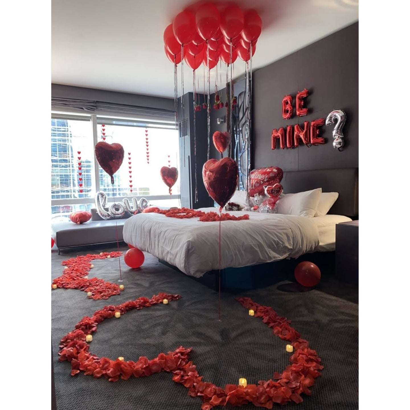 Decorated bedroom with red balloons, heart-shaped decorations, and 'Be Mine?' sign.
