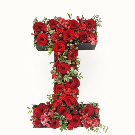 Floral arrangement shaped like the letter 'T' with red roses and green leaves 