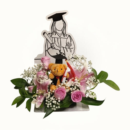 Graduation-themed floral arrangement with a teddy bear and decorative elements on a white background