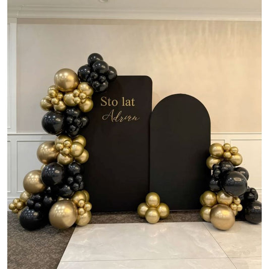 Balloon arches in black and gold with decorative text on a plain wall.