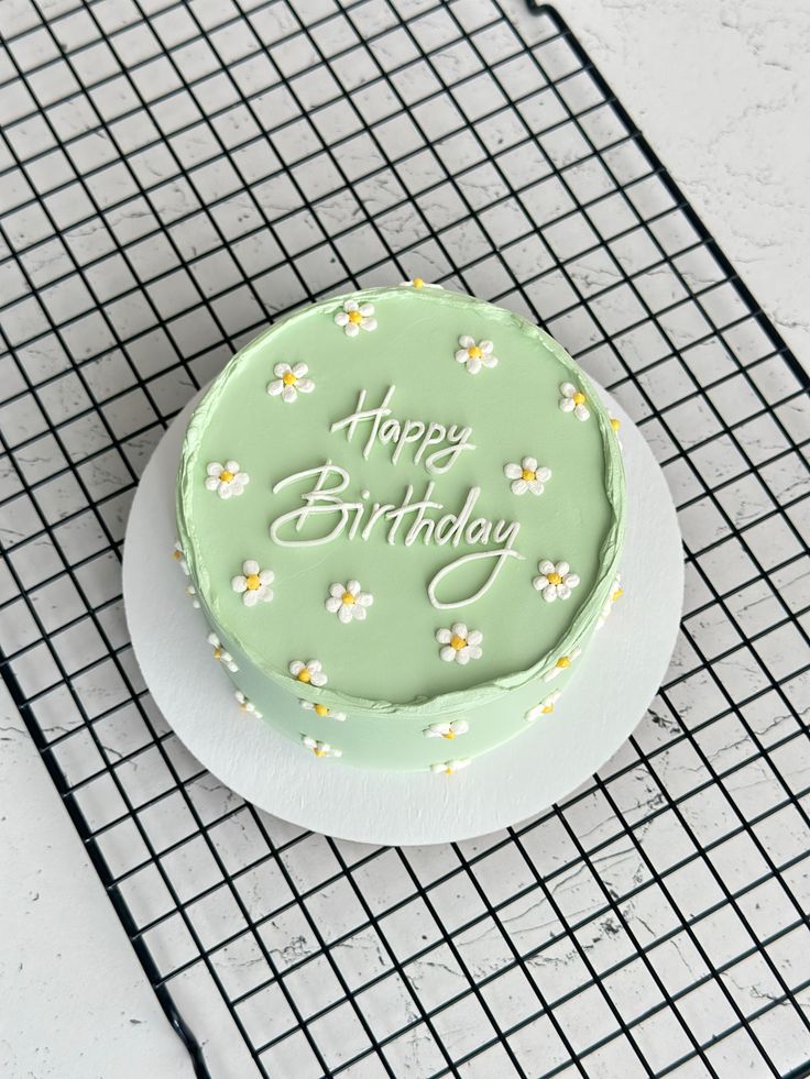 Green birthday cake with 'Happy Birthday' text on a cooling rack

