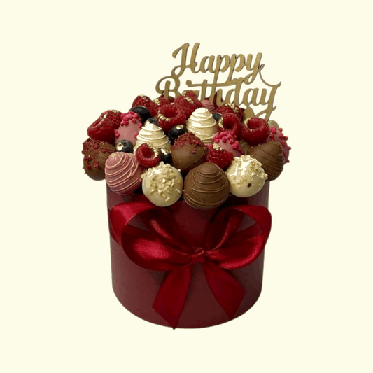 Bouquet of chocolates and berries in a red box with a 'Happy Birthday' topper on a beige background