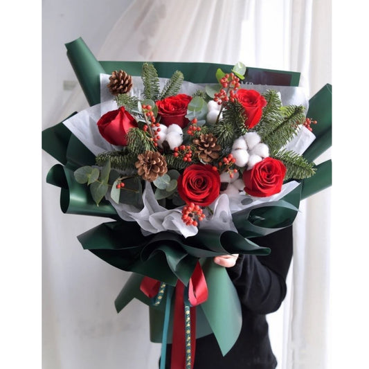Bouquet of red roses with greenery and decorative ribbons held by a person.