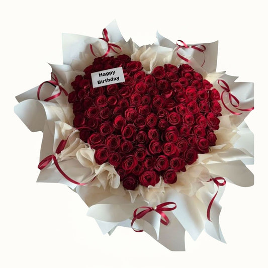 Heart-shaped bouquet of red roses with white paper and red ribbons on a white background