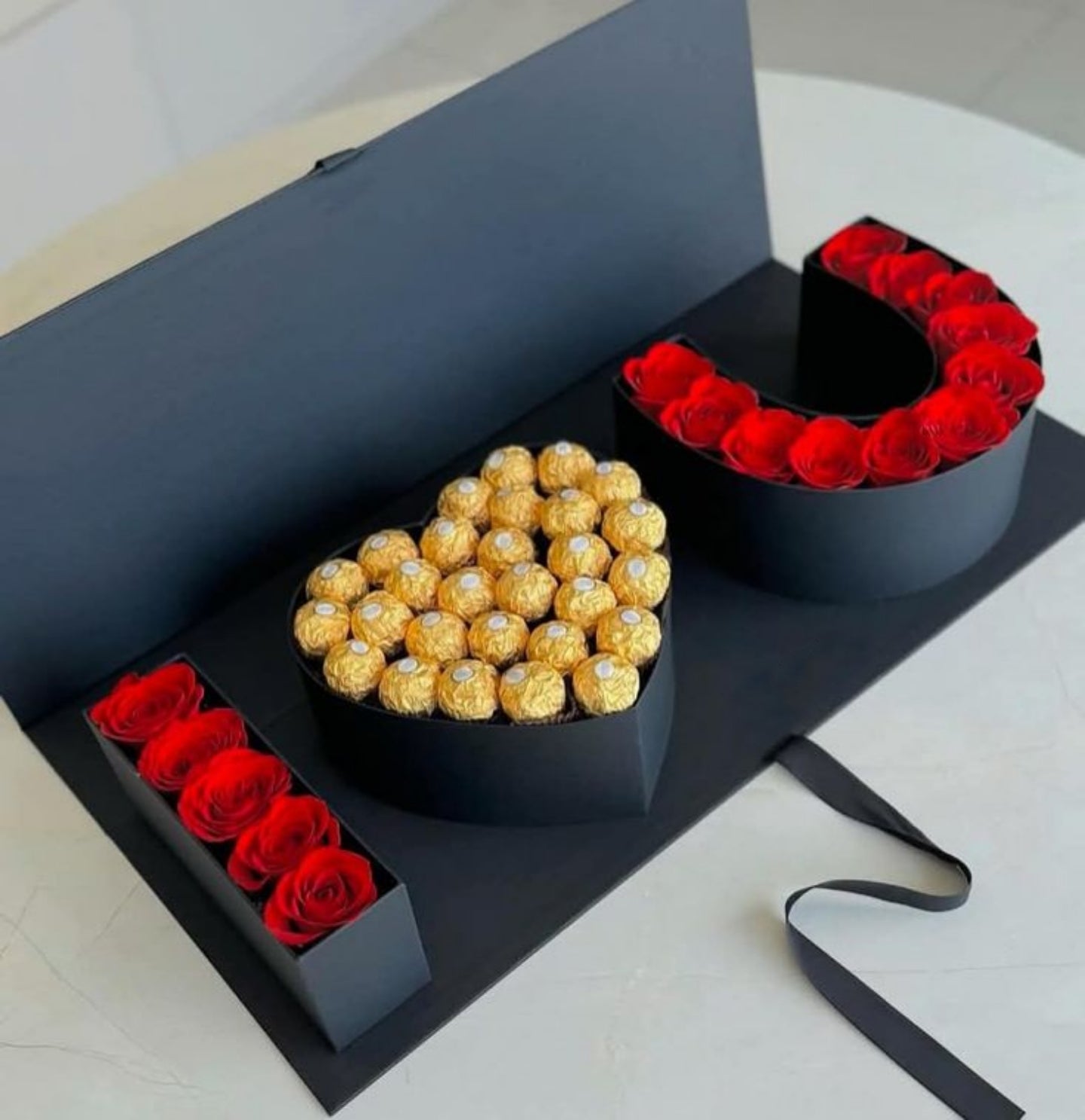 Heart-shaped box with gold Ferrero Rocher chocolates and red roses on a white surface.
