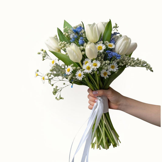Bouquet of white tulips, blue flowers, and daisies held by a hand on a white background
