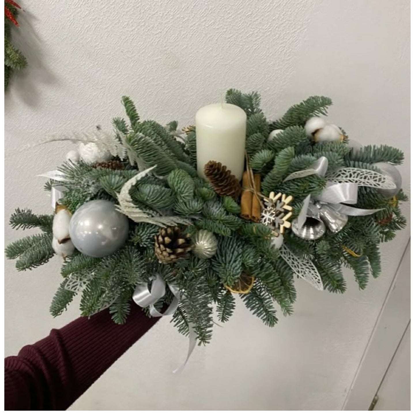 Decorative Christmas wreath with candles, ornaments, and ribbons on a white wall.