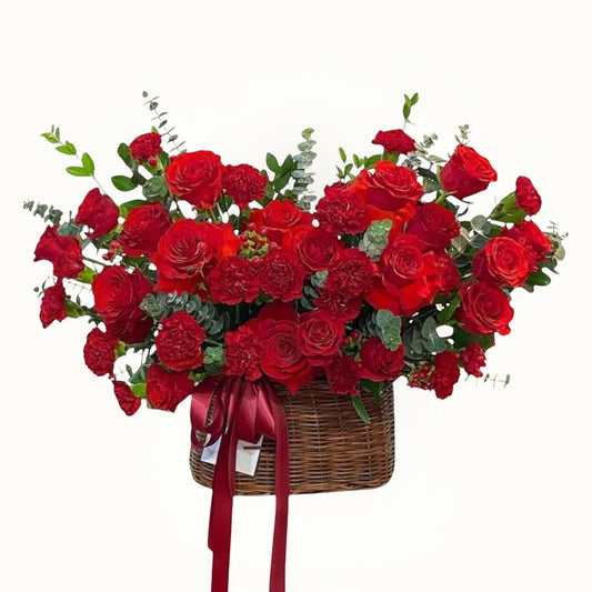 Bouquet of red roses in a basket with greenery on a white background