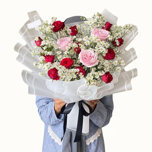 Bouquet of red and pink roses with white flowers held by a person on a white background