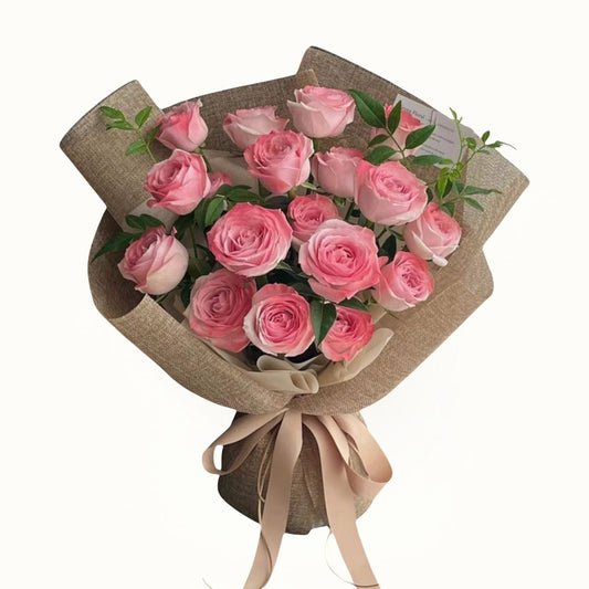 Bouquet of pink roses wrapped in brown paper with a beige ribbon on a white background