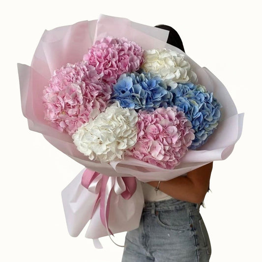 Bouquet of pink, blue, and white flowers held by a person wearing jeans.