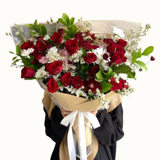 Bouquet of red and white flowers with greenery, held by a person wearing a black coat.