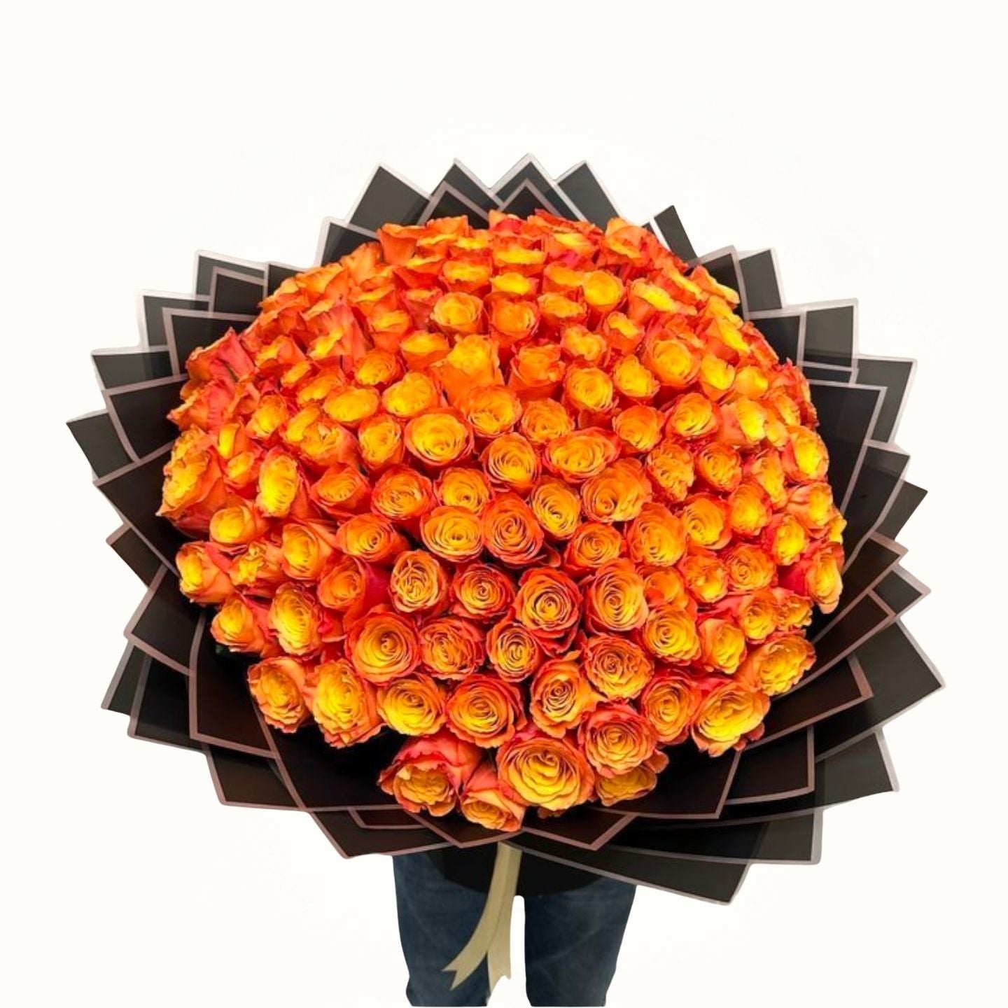 Bouquet of orange and yellow roses wrapped in black paper held by a person.