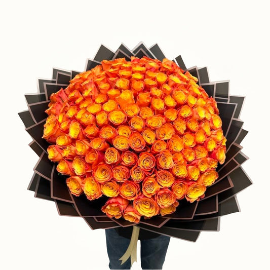 Bouquet of orange and yellow roses wrapped in black paper held by a person.