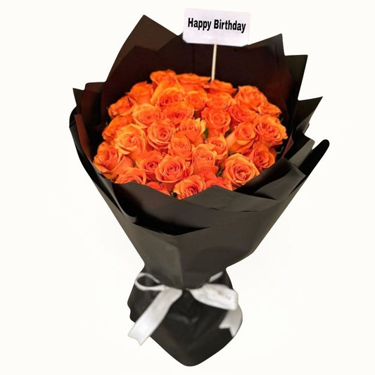 Bouquet of orange roses wrapped in black paper with a 'Happy Birthday' tag on a white background