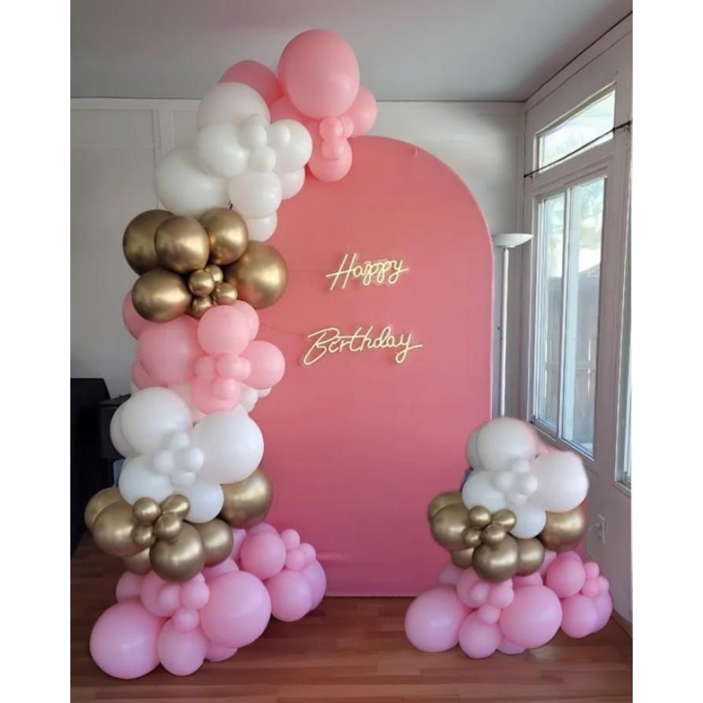 Balloon arch with pink, gold, and white balloons against a pink wall with 'Happy Birthday' text.