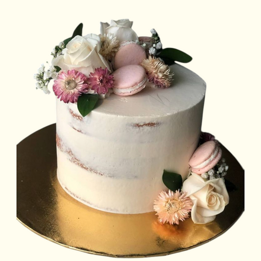 White cake with pink flowers and macarons on a gold stand