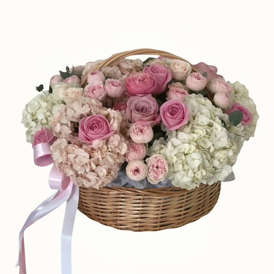 Bouquet of pink and white flowers in a wicker basket with ribbons on a white background